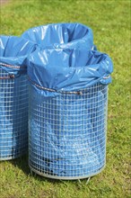 Rubbish bins with blue rubbish bags standing in a meadow, Germany, Europe