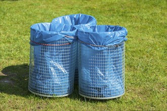 Rubbish bins with blue rubbish bags standing in a meadow, Germany, Europe