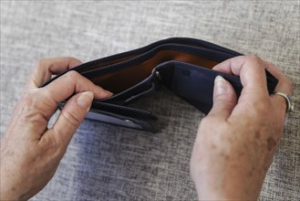 An elderly woman looks into her empty wallet. Berlin, 05.08.2024