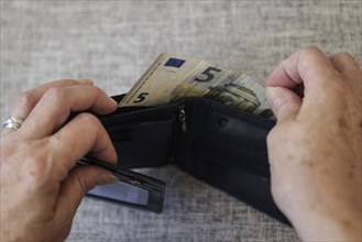 An elderly woman takes five euros out of her wallet. Berlin, 05.08.2024