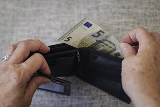 An elderly woman takes five euros out of her wallet. Berlin, 05.08.2024