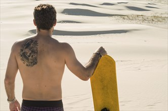 Young man on his back looking at the sand dunes, preparing to practice sandboarding