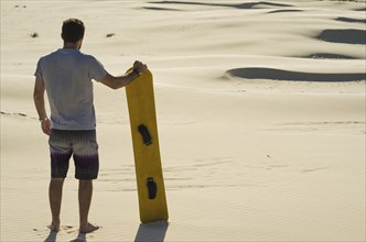 Young man on his back looking at the sand dunes, preparing to practice sandboarding