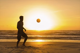 Great concept of soccer, man playing soccer on the beach in golden hour, sunset. Making keepie