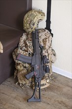 A military helmet and a rifle lie on a camouflaged rucksack on a wooden floor, mobilisation,