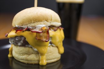 Close-up of tasty homemade bacon burger and cheddar sauce on wooden table and black background