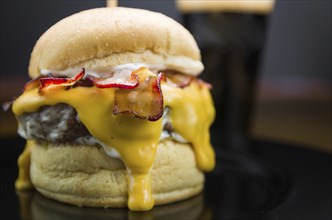 Close-up of tasty homemade bacon burger and cheddar sauce on wooden table and black background