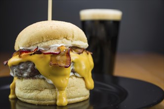 Close-up of tasty homemade bacon burger and cheddar sauce on wooden table and black background