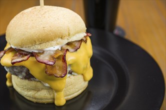 Close-up of tasty homemade bacon burger and cheddar sauce on wooden table and black background