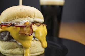 Close-up of tasty homemade bacon burger and cheddar sauce on wooden table and black background