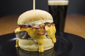 Close-up of tasty homemade bacon burger and cheddar sauce on wooden table and black background