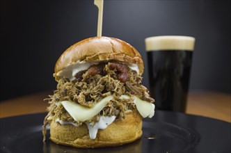 Close-up of tasty homemade pulled pork burger on wooden table and black background