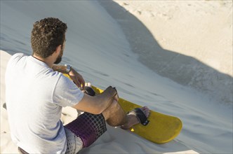 Young man on his back looking at the sand dunes, preparing to practice sandboarding