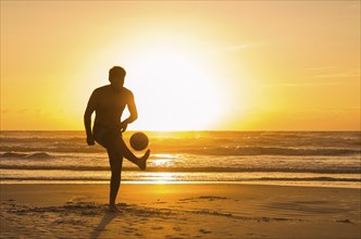 Great concept of soccer, man playing soccer on the beach in golden hour, sunset. Making keepie