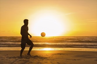 Great concept of soccer, man playing soccer on the beach in golden hour, sunset. Making keepie