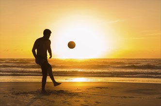 Great concept of soccer, man playing soccer on the beach in golden hour, sunset. Making keepie