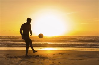 Great concept of soccer, man playing soccer on the beach in golden hour, sunset. Making keepie