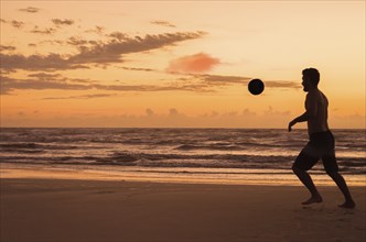 Great concept of soccer, man playing soccer on the beach in golden hour, sunset. Making keepie