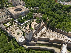 Aerial view of a castle complex with surrounding wall, surrounded by green vegetation and urban