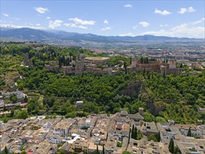 Aerial view of a castle in green surroundings with a town, hills and mountains in the background,