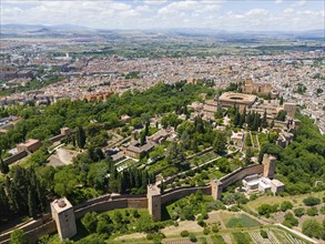 Aerial view of a castle complex surrounded by green trees and bordering an urban landscape with