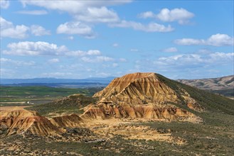 View of a large rocky hill with valley floor under a blue sky with clouds, Bardenas Reales Natural