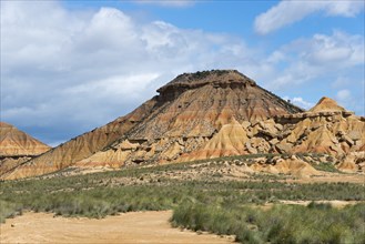 Rocky hill in an arid landscape under a blue sky with clouds, Bardenas Reales Natural Park, desert,