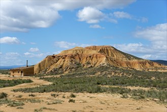 Small building in front of a rocky hill in an arid landscape under a cloudy sky, Bardenas Reales