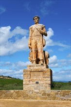 Statue of a pastor on a pedestal in front of a blue sky with clouds, green fields in the