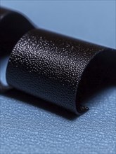 Glossy black ribbon loop with a textured surface on a blue background, AI generated