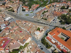 Aerial view of a city crossed by a long, historic aqueduct, surrounded by tiled roofs and street