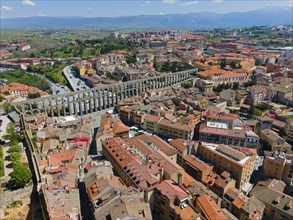 Aerial view of a city with a striking aqueduct and many historic buildings with red tiled roofs,