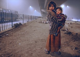 New Delhi, India, 21.01.2010, A homeless girl holds her sister in her arms. She and her family are