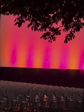 Empty rows of seats in the open-air cinema in front of a brightly lit stage, illuminated in red and