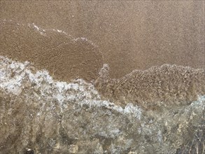 Waves breaking on the coast, leaving a texture on wet sand