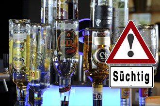 Alcohol bottles in a bar with a warning sign about the danger of addiction, illuminated with neon