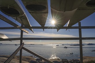 Traditional kayaks on wooden frame in front of icebergs, sun star, summer, Inuit, Ilulissat,