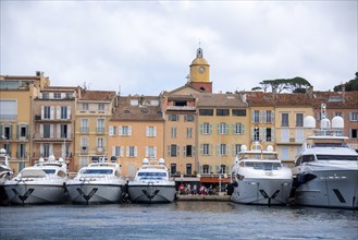 Yachts moored in the harbour of Saint Tropez, behind them colourful houses and the Notre-Dame de