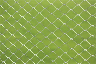 Mesh screen made of interwoven metal cables. The background is a uniform green colour. This image