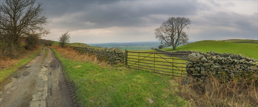 View of the English countryside along a stone wall with a gate and adjacent country lane and a