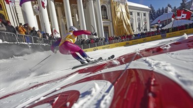 Ski racer speeding down a slope towards the finish line while a crowd watches during a winter