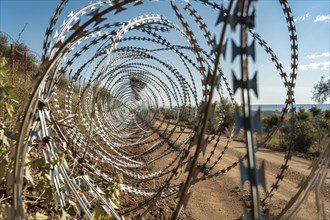 View through spiraled barbed wire fencing along a path under a clear sky, AI generated