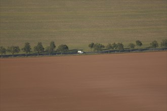 View from Kyffhäuser monument to straight road with avenue and white car, view from above, fields,