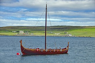 A traditional Viking boat with shields on the calm water, overlooking a green coastline and hills