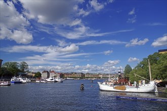 View of a harbour full of ships under a blue sky with clouds and a city panorama on the water,