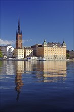 Picturesque view of a church tower and historic buildings along a calm shore with clear water