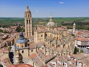 Aerial view of a historic city with a large church and red roofs under a clear blue sky, surrounded