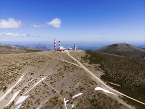 Transmitters on a hilly mountain under a clear blue sky with scattered clouds, aerial view, Bola