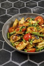 Close-up view of fried ravioli with green beans, tomato and champignon mushrooms in a plate