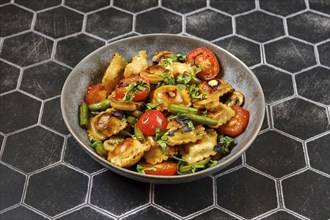 Fried ravioli with green beans, tomato and champignon mushrooms in a plate